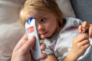 Parent takes temperature for her child with infrared thermometer at home, high fever